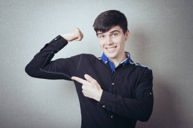 Bir adam işaret parmağını el kaslarında güçlü gösterir. Gri bir arkaplanda.