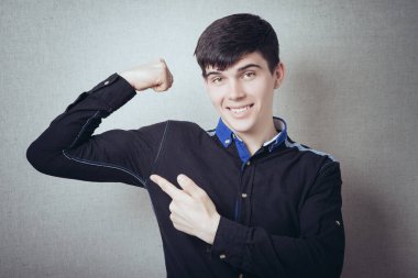 Bir adam işaret parmağını el kaslarında güçlü gösterir. Gri bir arkaplanda.