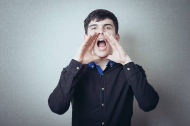 Elleri ağzının yanında olan bir adam. Birini çağırmak için işaret et, yüksek sesle konuş. Gri bir arkaplanda