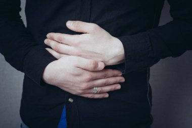 Elleri karnında, karnı ağrıyor. Jest karın ağrısı, kramplar. Gri bir arkaplanda