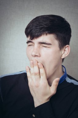 Bir adam uykulu, iş yerinde yorgun esniyor. Gri bir arkaplanda.