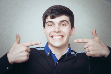 Adam dişlerini göstererek gülümsüyor. Dişçiden sonra sağlıklı dişler. Gri bir arkaplanda.
