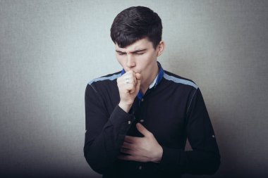 Erkek hasta öksürüyor. Gri bir arkaplanda.