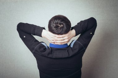 Gri bir arka plan üzerinde elleri kafasında genç bir adamın arka görüntüsü