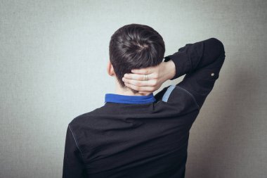 Gri bir arka plan üzerinde elleri kafasında genç bir adamın arka görüntüsü