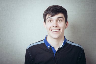 İnanılır gibi değil! Şok olmuş genç adam gri arka planda dururken alaycı bir gülümseme sergiliyor.