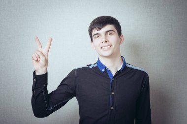 Genç adam kameraya gülümserken zafer jestini gösteriyor. 