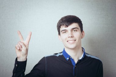 Genç adam kameraya gülümserken zafer jestini gösteriyor. 