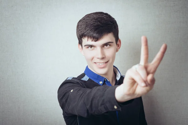 Ein Junger Mann Macht Eine Siegesgeste Auf Grauem Hintergrund — Stockfoto