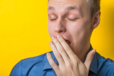 Yakışıklı genç adam esniyor. Yakın plan portre. Jest yap. İzole edilmiş sarı arka plan. fotoğraf