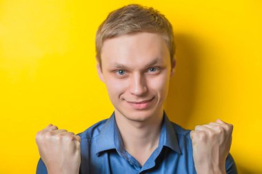 Yumruklarını tutan, destekleyen yakışıklı bir genç. Kapalı portre. Senin jestine katılıyorum. İzole edilmiş sarı arka plan. fotoğraf