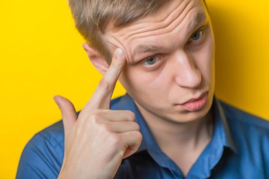 Sarışın genç adam parmağını şakağına dayayıp ne yapacağını düşünüyor. Kapalı portre. Jest yap. İzole edilmiş sarı arka plan. fotoğraf