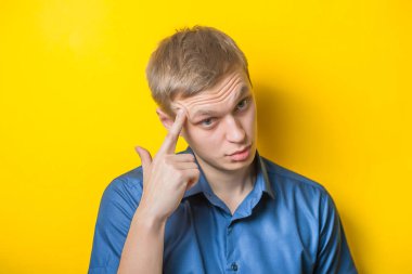Sarışın genç adam parmağını şakağına dayayıp ne yapacağını düşünüyor. Kapalı portre. Jest yap. İzole edilmiş sarı arka plan. fotoğraf