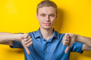 Yakışıklı genç adam başparmağını aşağı indirerek yumruğunu indirdi. Kapalı portre. Hoşnutsuz bir jest. İzole edilmiş sarı arka plan. fotoğraf