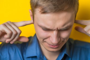 Sarışın genç adam, senden haber almak istemediğini gösteriyor. Parmakları kulaklarında. Jest. Kapalı portre. İzole edilmiş sarı arka plan. fotoğraf