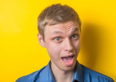 Genç, ciddi, sarı arka planda mavi gömlekli sarışın bir adam. Seni gördüğüme ne kadar sevindim. Gülümse. Jest yap. Fotoğraf Çekimi.