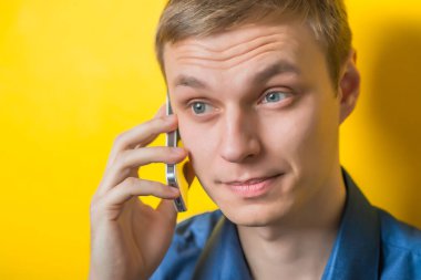 Sarışın genç adam telefonda konuşuyor. Jest yap. İzole edilmiş sarı arkaplan.