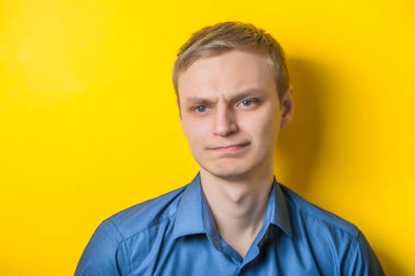 Sarı arka planda mavi gömlekli genç sarışın adam. Düşünce olarak, mutsuz. Jest yap. Fotoğraf Çekimi.