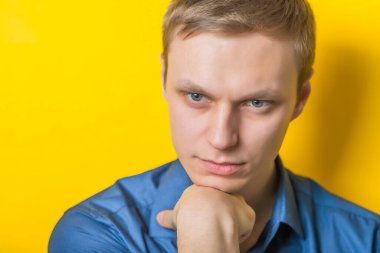 Sarışın genç adam düşünüyor. Kafası elinde dinleniyor, kameraya bakıyor. Jest yap. İzole edilmiş sarı arkaplan.