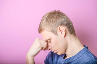 Genç adam düşünüyor. Kafasını eline koy. Profil. Jest yap. Mor bir arka planda.