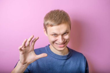 Genç adam gülümsemekten korkuyor, şaka yapıyor. Jest yap. Mor bir arka planda.