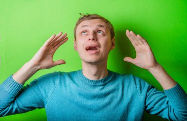 Genç adam yukarı bakıyor, ellerini havaya kaldırıyor.