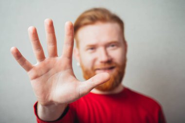 Genç adam el sallıyor, gülümsüyor.