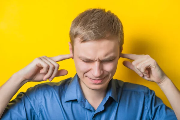 Blond young man shows he does not want to hear from you. Fingers in his ears. gesture. Close portrait. Isolated yellow background. photo