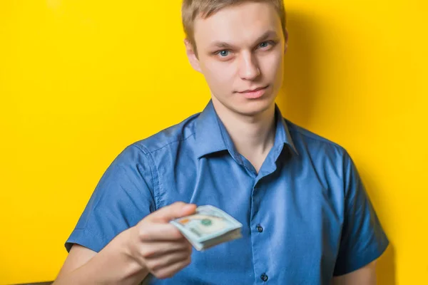 黄色の背景に青いシャツを着た若い男がお金を与えるか取る ドルだ 手に金を持っている そうだ — ストック写真