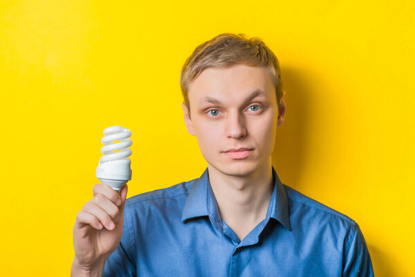 smiling casual man holding a energy-saving lightbulb isolated on yellow background