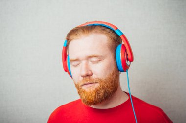 Kulaklıkla şarkı söyleyen ve müzik dinleyen genç kızıl sakallı bir adamın portresi. 