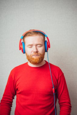 Kulaklıkla şarkı söyleyen ve müzik dinleyen genç kızıl sakallı bir adamın portresi. 