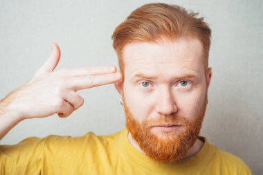 Sarı tişörtlü, sakallı, gri arka planlı bir adam.
