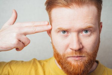 Sarı tişörtlü, sakallı, gri arka planlı bir adam.