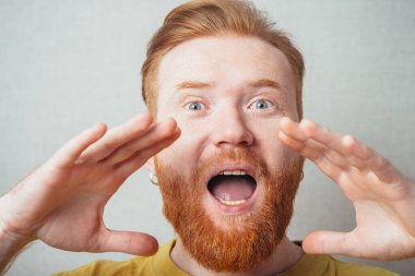 Sarı tişörtlü, sakallı, gri arka planlı bir adam birini arıyor.