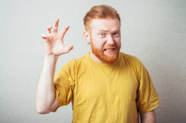 Aslan gibi sarı tişörtlü, sakallı, gri arka planlı bir adam.