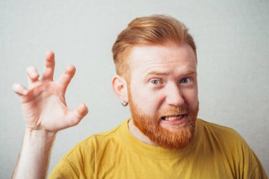 Aslan gibi sarı tişörtlü, sakallı, gri arka planlı bir adam.