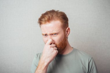 Tiksinmiş suratlı bir adam parmaklarıyla burun deliklerini kapatıyor.