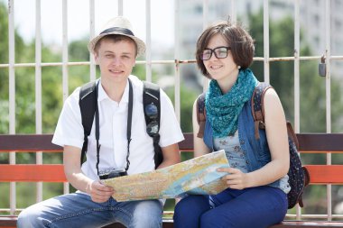 Mutlu genç turist çift bankta oturup haritayı inceliyor.