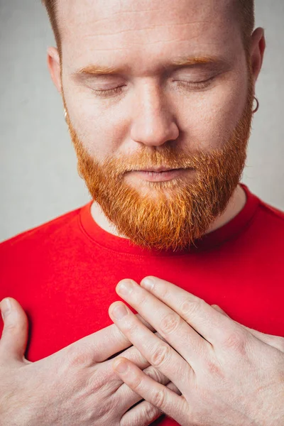Young red bearded Man holding his hand on his chest