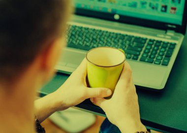 Bir kahve dükkanında dizüstü bilgisayarı üzerinde çalışan genç bir adamın kırpılmış görüntüsü, iş adamının elleri ofis masasında dizüstü bilgisayarla meşgul, genç bir erkek öğrenci ahşap masada oturuyor.