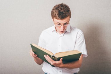 Gözlüklü adam büyük bir kitap okuyor.