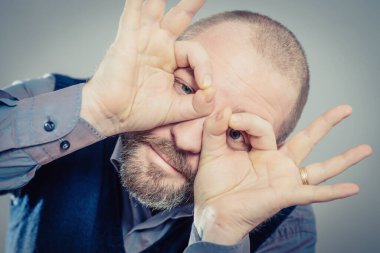 Elleri gözlerinde, parmaklarından bakan komik bir adam.