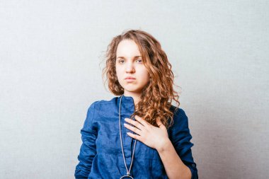 Kıvırcık kadın elini göğsüne koyar, kalbine. Gri arkaplan.