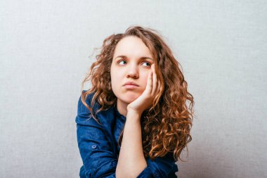 Kıvırcık kız üzgün düşünüyor. Kafasındaki el. Gri arkaplan.