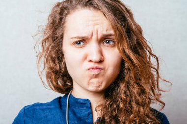 Kıvırcık kadın buruşuk suratlı mutsuz. Gri arkaplan.