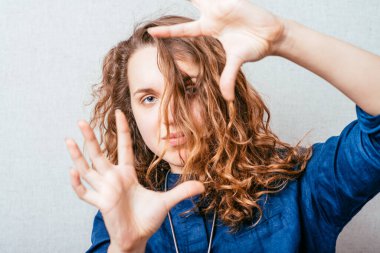 Kıvırcık kız parmaklarının arasından bakıyor. Gri arkaplan.