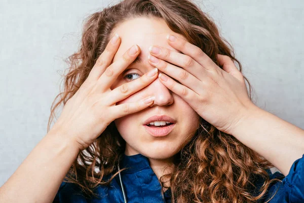 Een Krullend Meisje Kijkt Door Vingers Grijze Achtergrond — Stockfoto