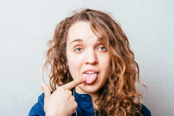 Krullend Meisje Toont Wijsvinger Tong Grijze Achtergrond — Stockfoto