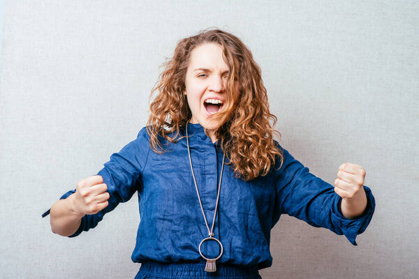 Curly woman showing a victory fist. Gray background.